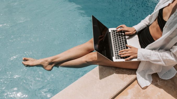 woman sitting on poolside using laptop